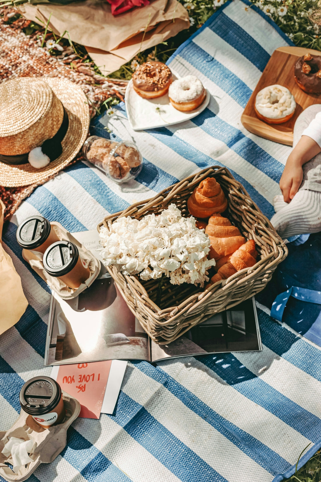 A picnic with croissants, donuts, and coffee on a blue and white striped blanket