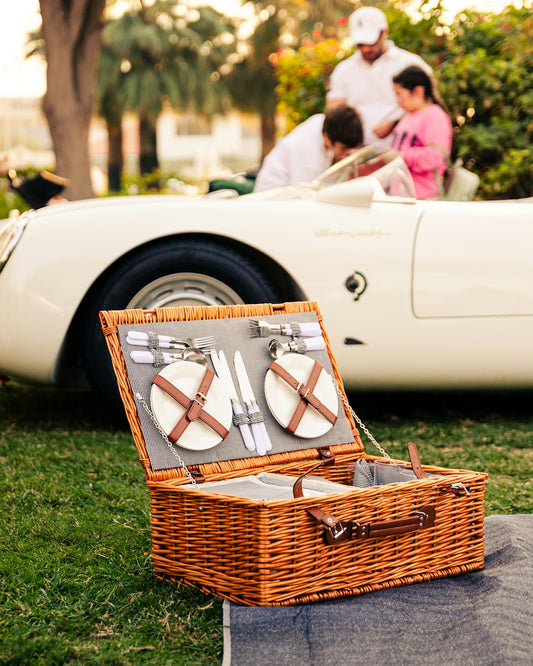 a wicker picnic basket with utensils in front of a white sports car
