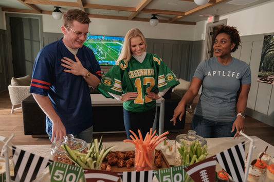 Friends in football jerseys gather around a snack table.