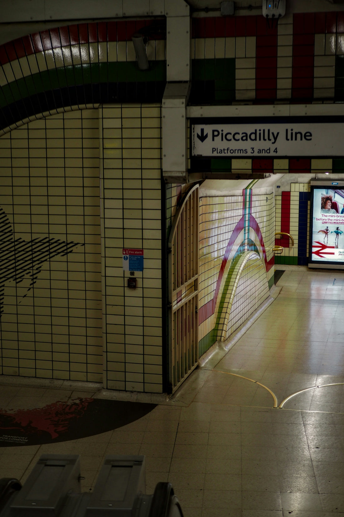 A Piccadilly line subway station platform with tiled walls and directional signage