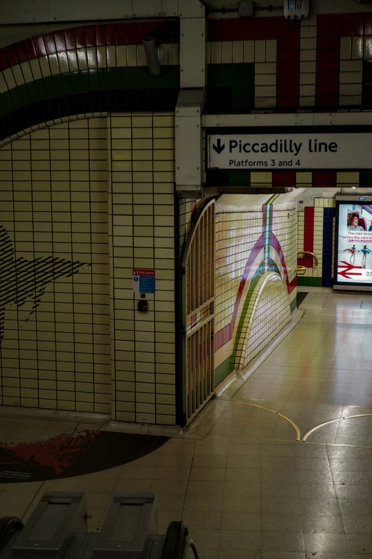 A Piccadilly line subway station platform with tiled walls and directional signage